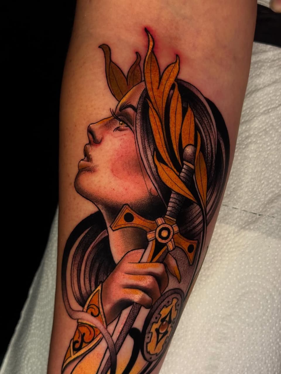 Portrait of a figure with flame-like hair holding a decorative weapon, rendered in orange, black, and brown tones on the forearm.
