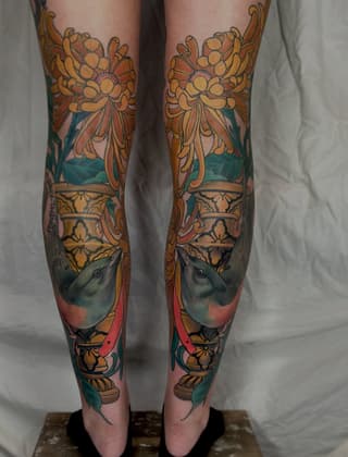 Matching leg tattoos featuring ornate floral urns with bird portraits, rendered in gold, teal, and coral colors on both legs.