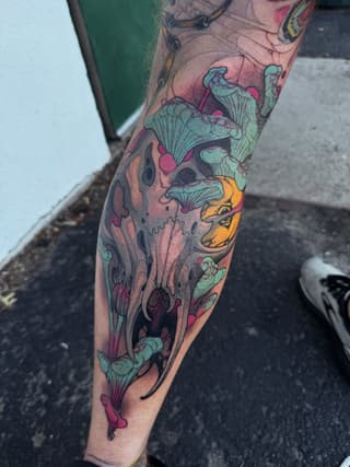 Colorful leg tattoo featuring anatomical skulls, mushrooms, and organic forms in turquoise, pink, orange, and purple tones on the calf and shin.