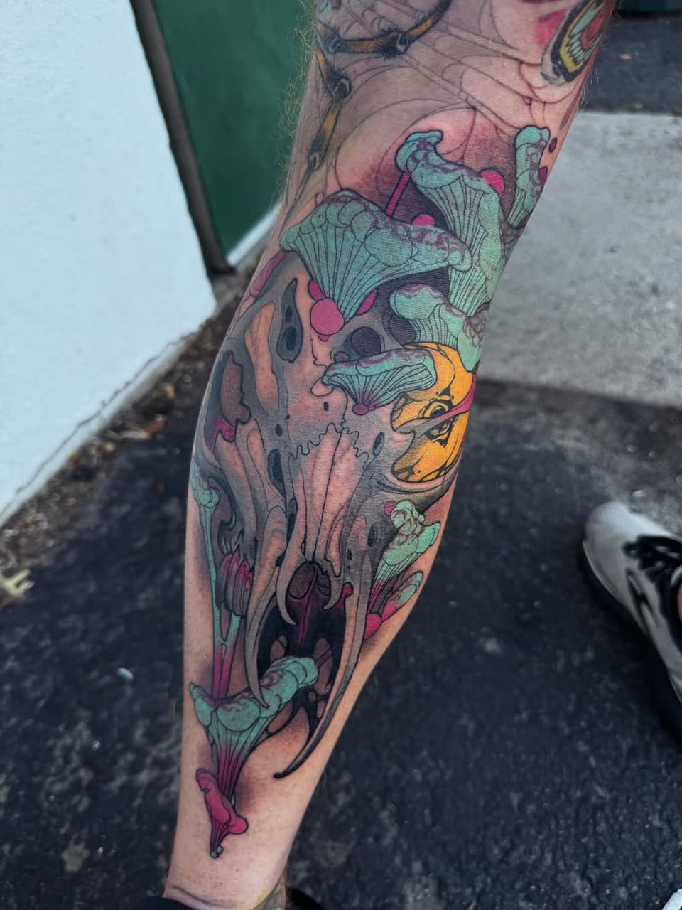 Colorful leg tattoo featuring anatomical skulls, mushrooms, and organic forms in turquoise, pink, orange, and purple tones on the calf and shin.