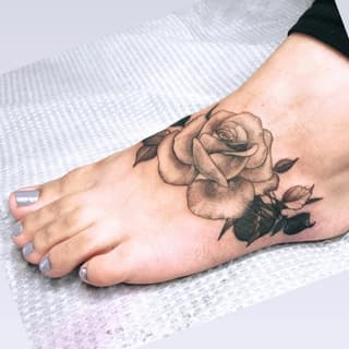 Rose with leaves and buds tattooed on the top of a foot in brown and black ink.