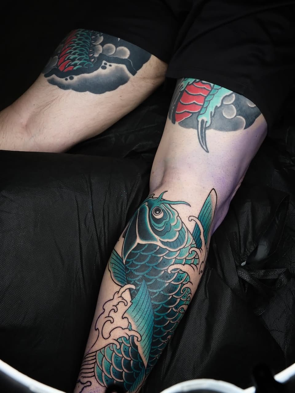 Two arms display koi fish tattoos in turquoise and red with clouds, waves, and moon phases in shades of blue, gray, and white.