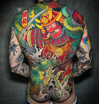 Colorful full-back tattoo featuring an ornate samurai warrior with dragon and floral motifs in red, green, yellow, and gold on bare skin.