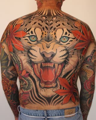 Back tattoo featuring a roaring leopard face with blue eyes and red flowers, covering the upper back and extending down both arms.