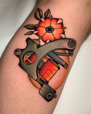 Tattoo on arm featuring a red flower with black leaves above a gray tattoo machine holding a red and orange grenade, colored in red, orange, and gray tones.