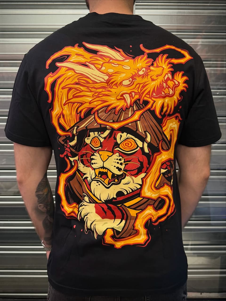 Back tattoo featuring a fierce tiger head with flames surrounding it in orange, yellow, and red tones on black fabric.
