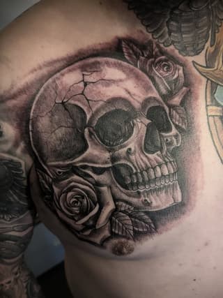 Skull with roses tattoo on upper chest and shoulder in grayscale with shading and detail work.
