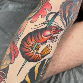 Colorful lobster tattoo on forearm with red, orange, black, and teal details, surrounded by decorative leaf and floral elements.