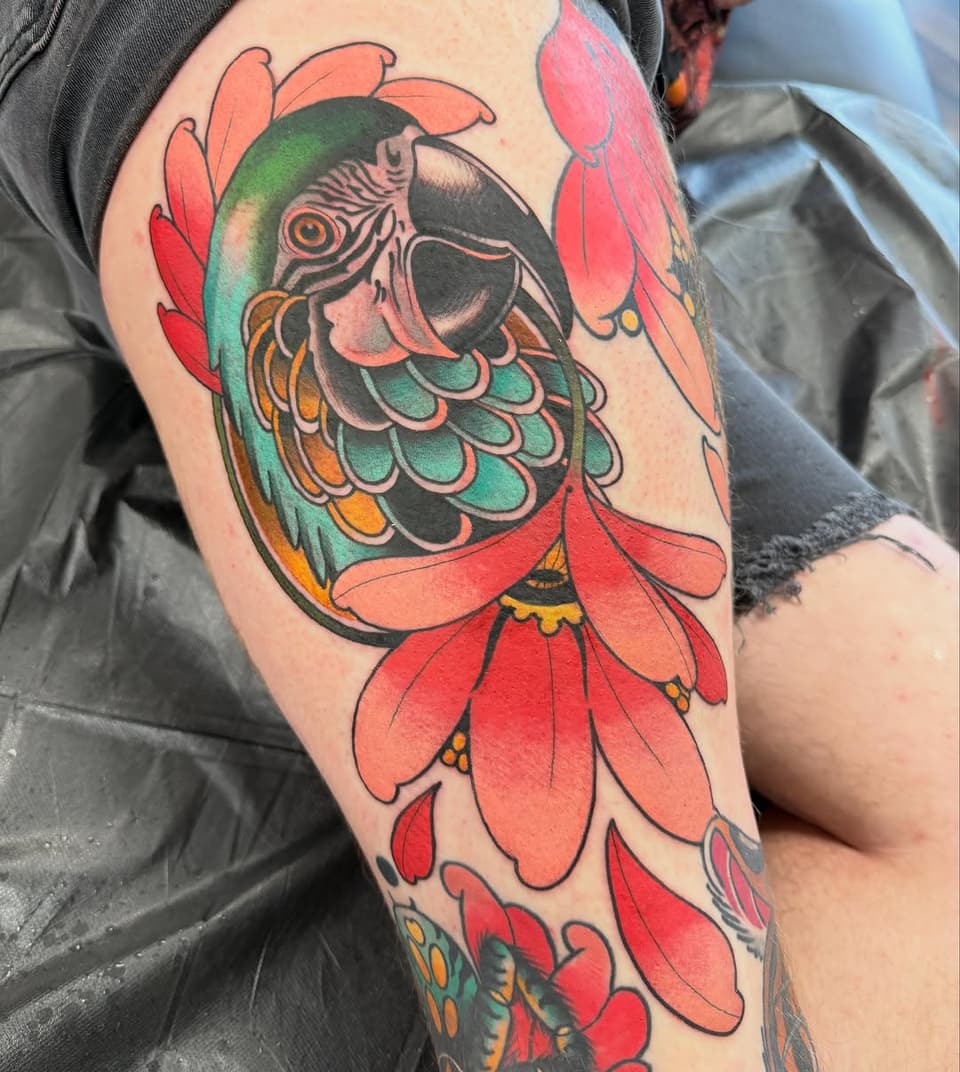 Colorful koi fish tattoo on upper arm featuring red petals, green and orange scales, black outlines, and gold accents.