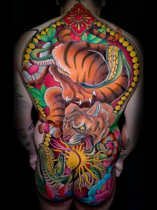Full back tattoo featuring two tigers with floral and decorative elements in orange, red, yellow, green, and blue colors.