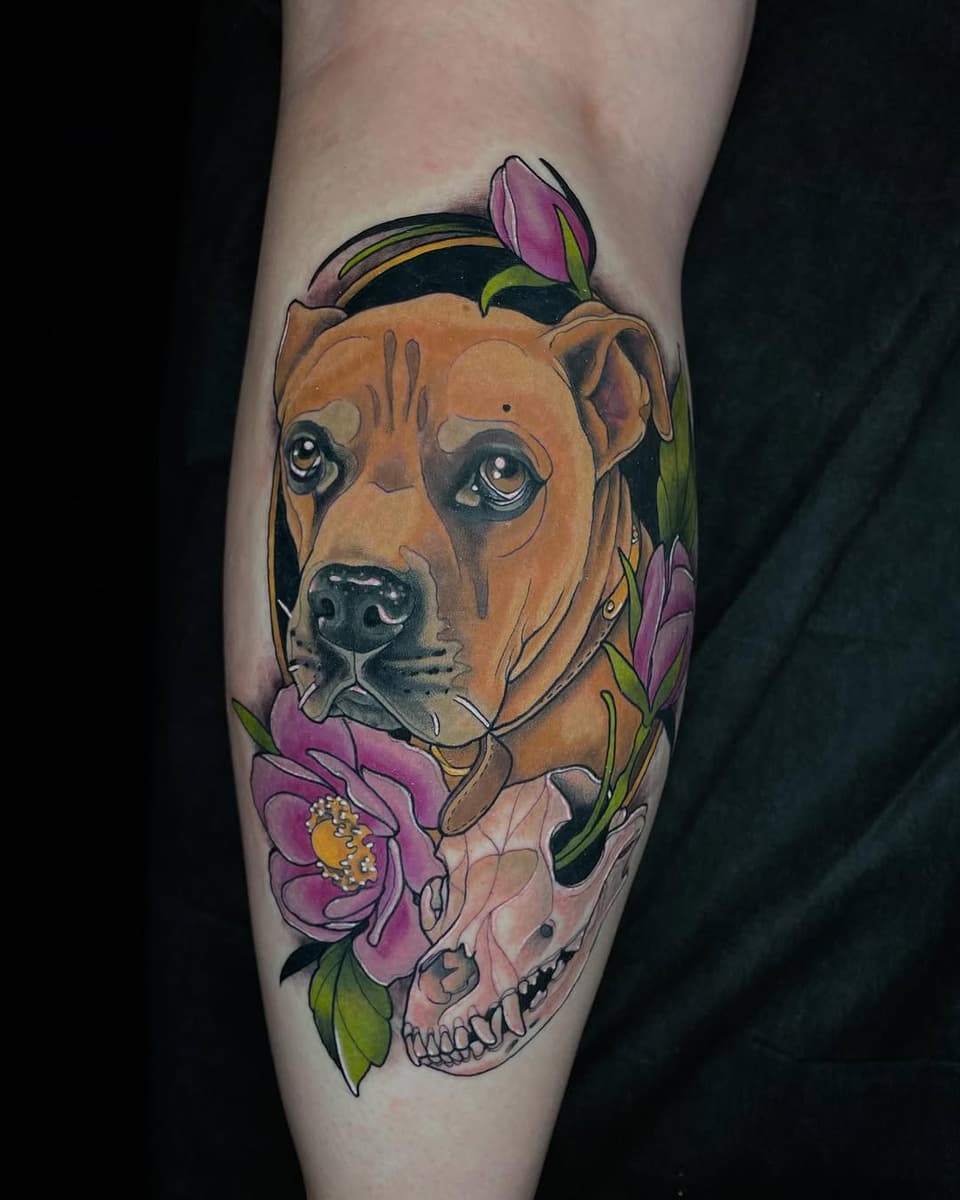Brown dog's head portrait with pink flowers and a skull integrated below, tattooed on a calf with orange, purple, green, and black colors.