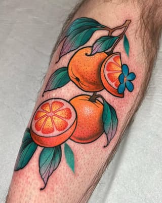 Colorful oranges and citrus slices with teal leaves and blue flowers tattooed on the forearm, featuring orange, red, and green hues.