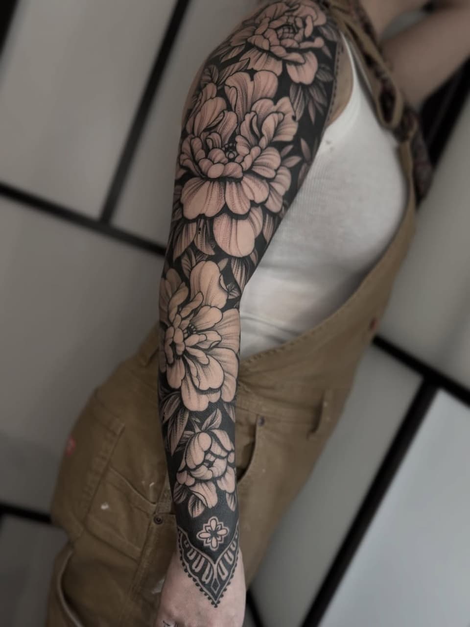 Full-sleeve floral tattoo featuring layered peonies and decorative elements in black ink on a person's arm.