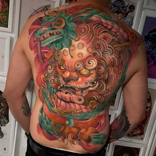 Large colorful back tattoo featuring a bearded face with ornate spiral hair, green foliage, and red background elements on a shirtless male torso.
