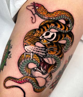 Colorful stacked tiger and serpent heads tattoo on upper arm featuring orange, black, and green scales with detailed facial features and open mouths.