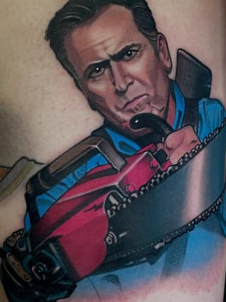 Colorful shoulder tattoo depicting a man with dark hair holding a red guitar, wearing a blue jacket with chain details.