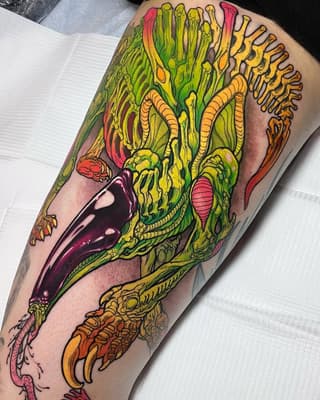 Colorful creature tattoo on calf featuring a green and yellow alien-like head with tentacles, red mouth, and orange clawed feet against tan skin.