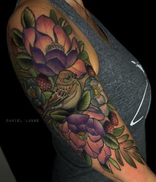Colorful shoulder tattoo featuring an owl surrounded by purple and pink flowers, green leaves, and red berries on brown skin.