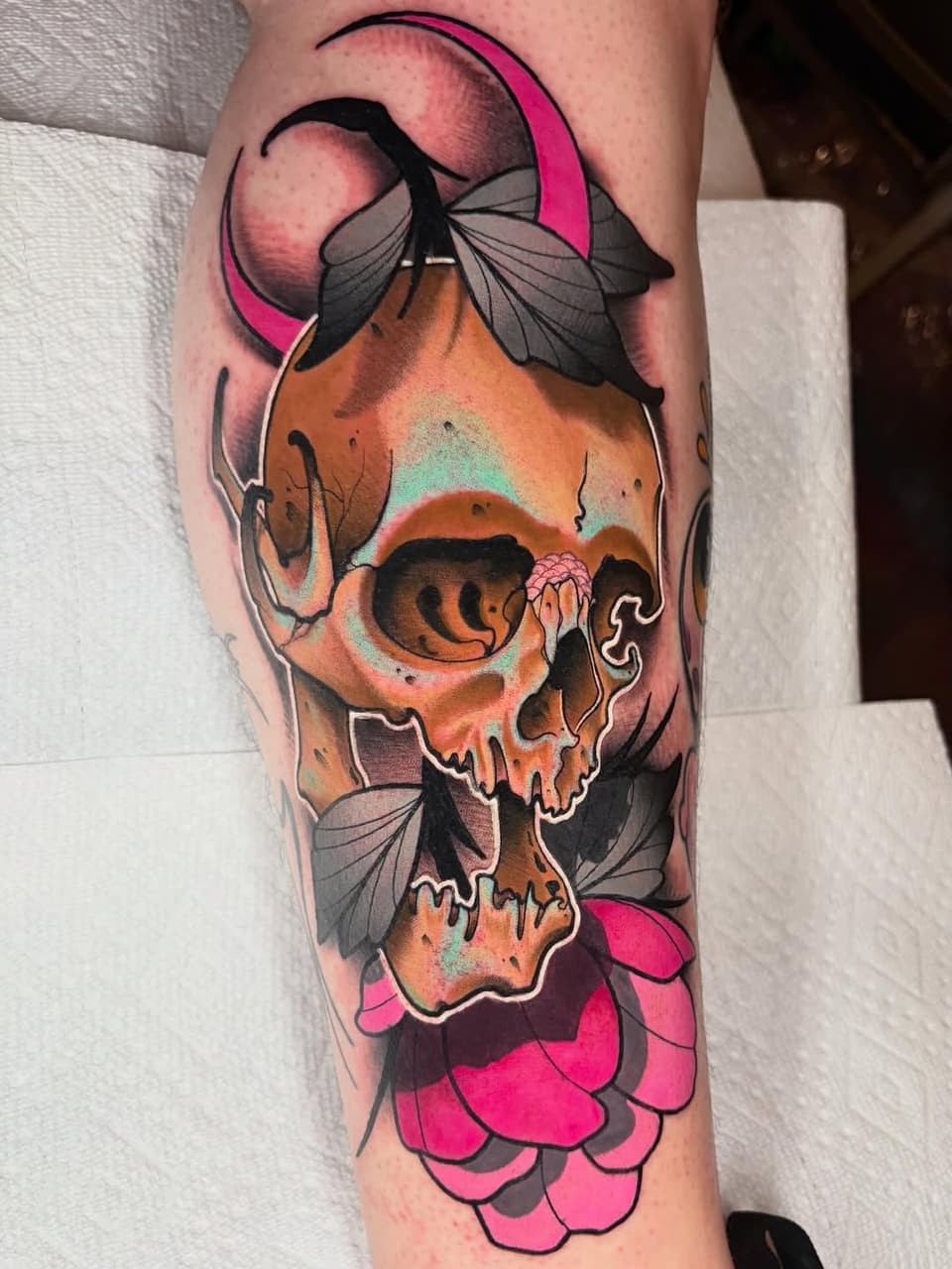 Colorful skull tattoo on forearm featuring orange and pink tones, with black-outlined butterflies and floral petals in magenta and gray.