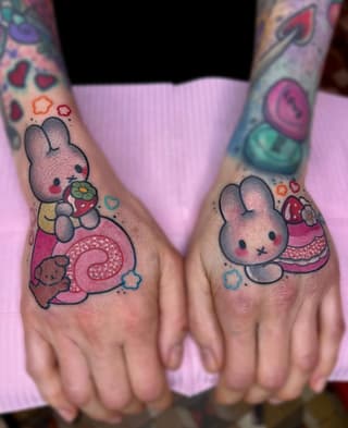 Colorful hand tattoos featuring gray bunnies holding strawberries and pastries surrounded by hearts and flowers in pink, red, and blue tones.