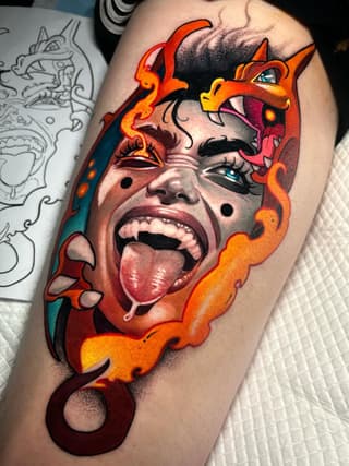 Colorful portrait tattoo on upper arm featuring a face with tongue out, surrounded by red and orange flame designs and decorative scrollwork elements.