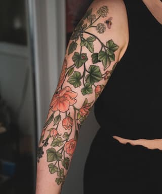 Full arm sleeve tattoo featuring coral flowers, green foliage, climbing vines, and a bumblebee on pale skin.