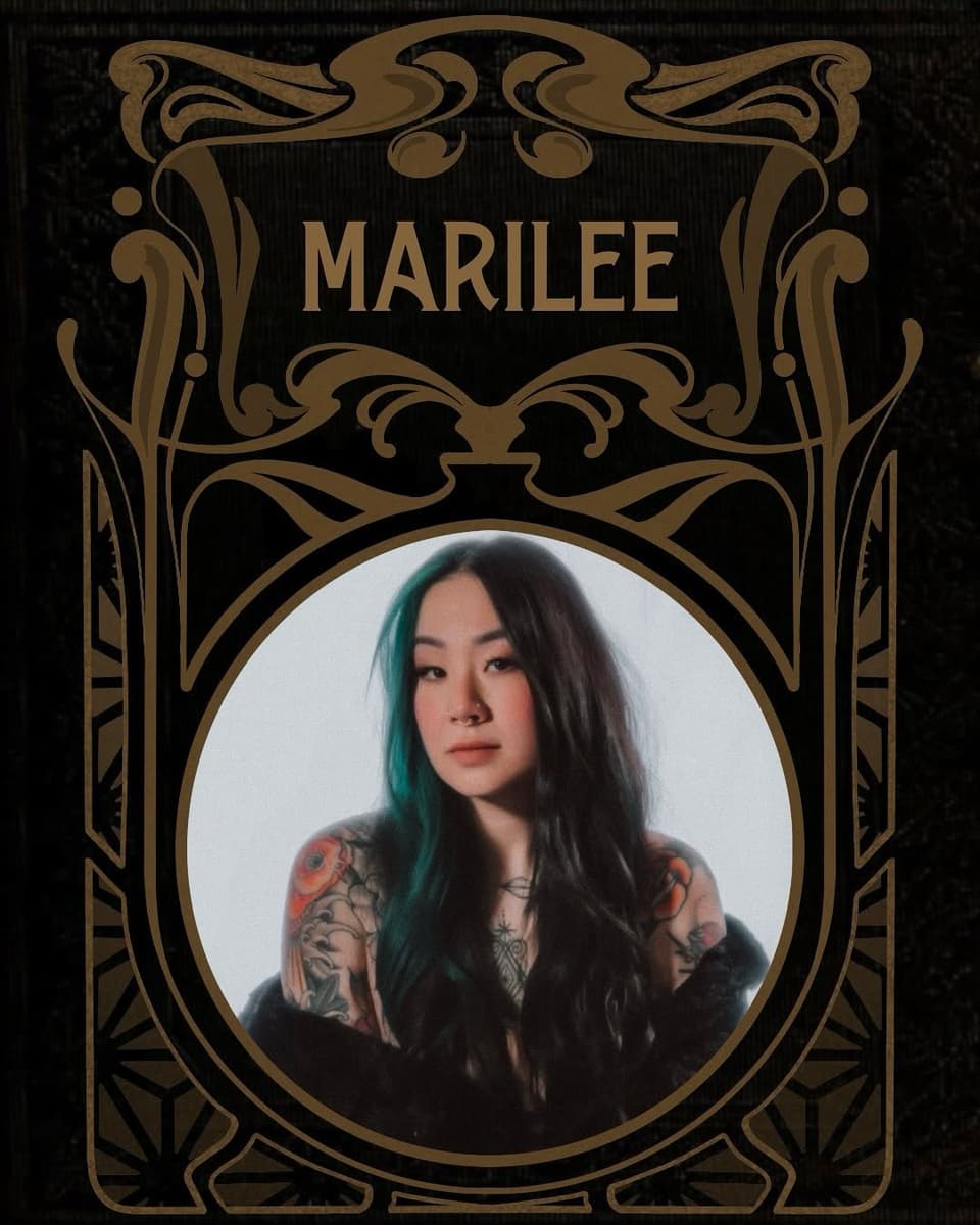 Portrait of a woman with long dark hair and teal streaks displaying colorful floral and geometric tattoos on both shoulders and arms.