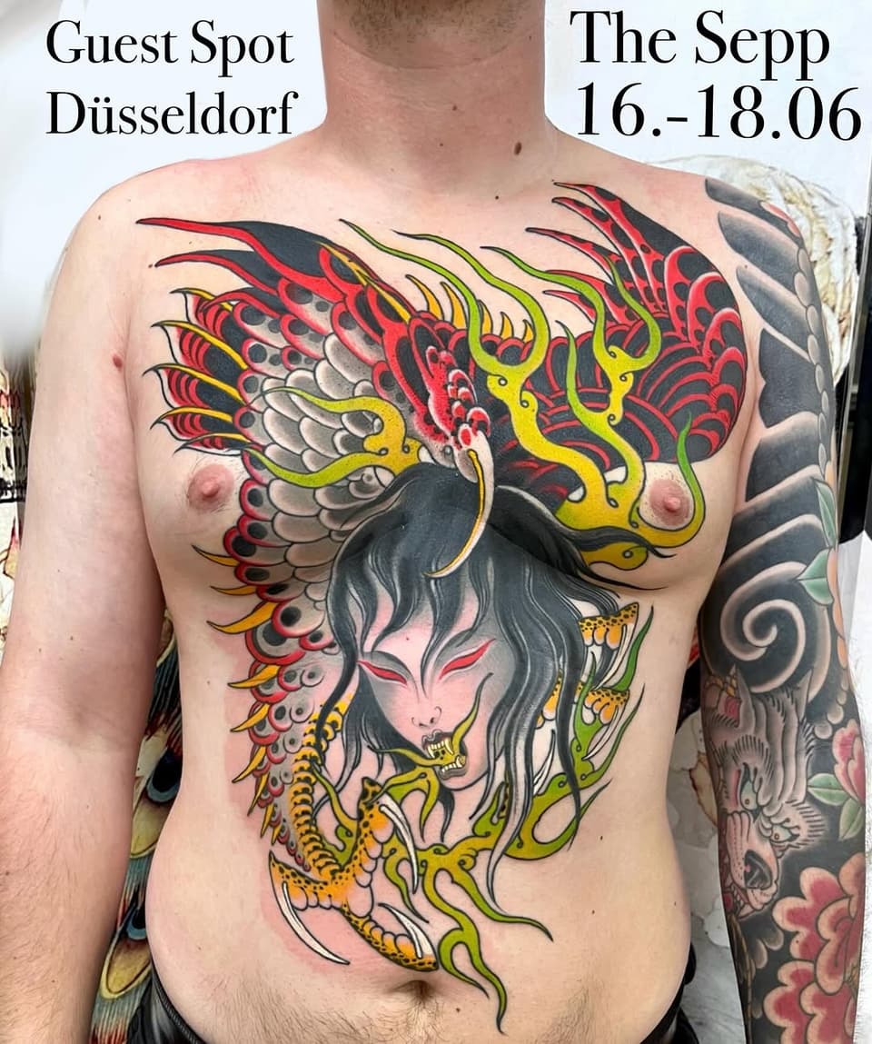 Colorful chest tattoo featuring a demon face with grey hair, yellow horns, red and black wings, and green serpentine elements across the torso.