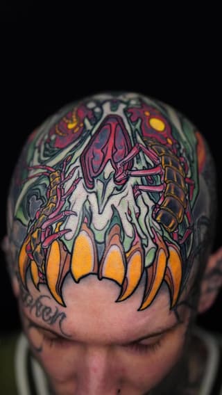 Colorful anatomical heart tattoo on back of head featuring red vessels, orange fangs, and detailed internal structures with yellow and green accents.