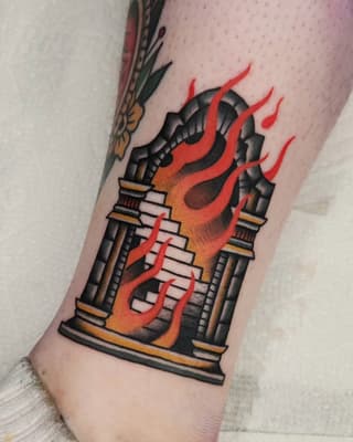 Burning building tattoo with red and orange flames, black architectural details, and gold accents on the upper leg.