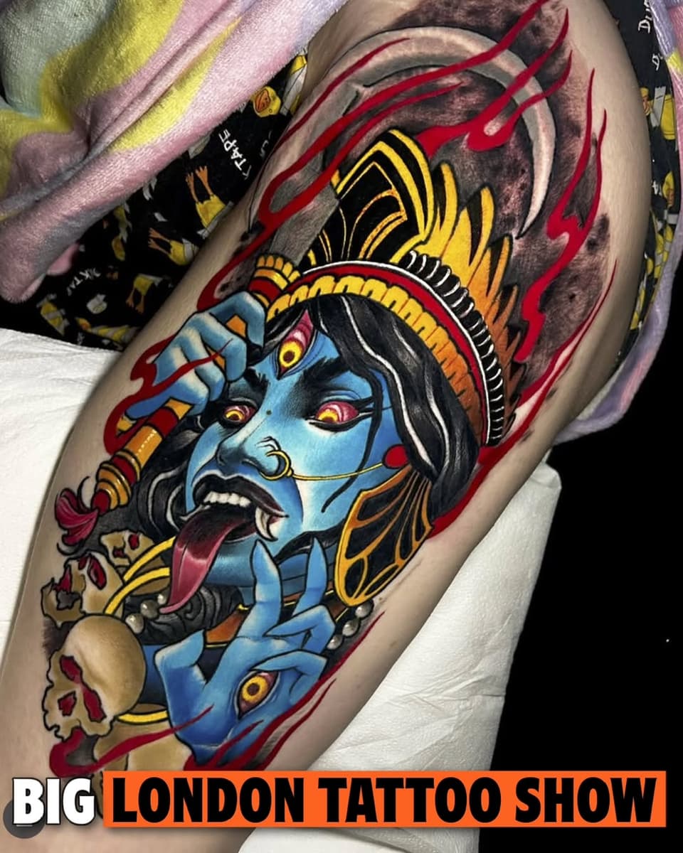 Colorful blue-faced deity head with red flames, golden crown, and ornamental details in red, yellow, and black on upper arm.