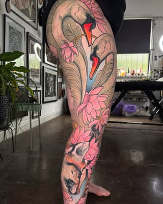 Full leg tattoo featuring stylized cranes and pink flowers with red and blue accents, displayed in a studio setting.