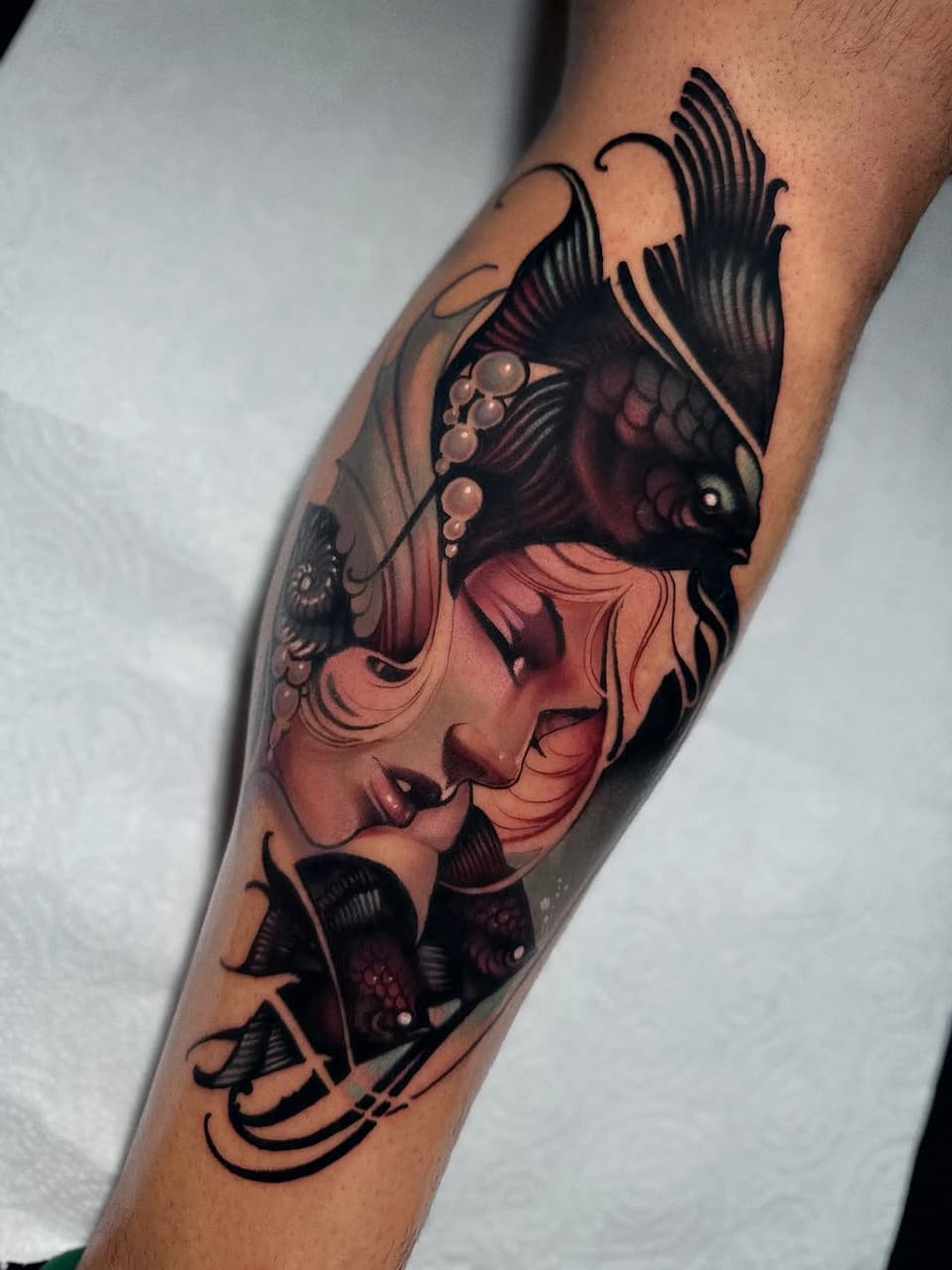Colorful leg tattoo featuring a woman's face with flowing hair and black fish swimming around her, rendered in coral, burgundy, and black tones.