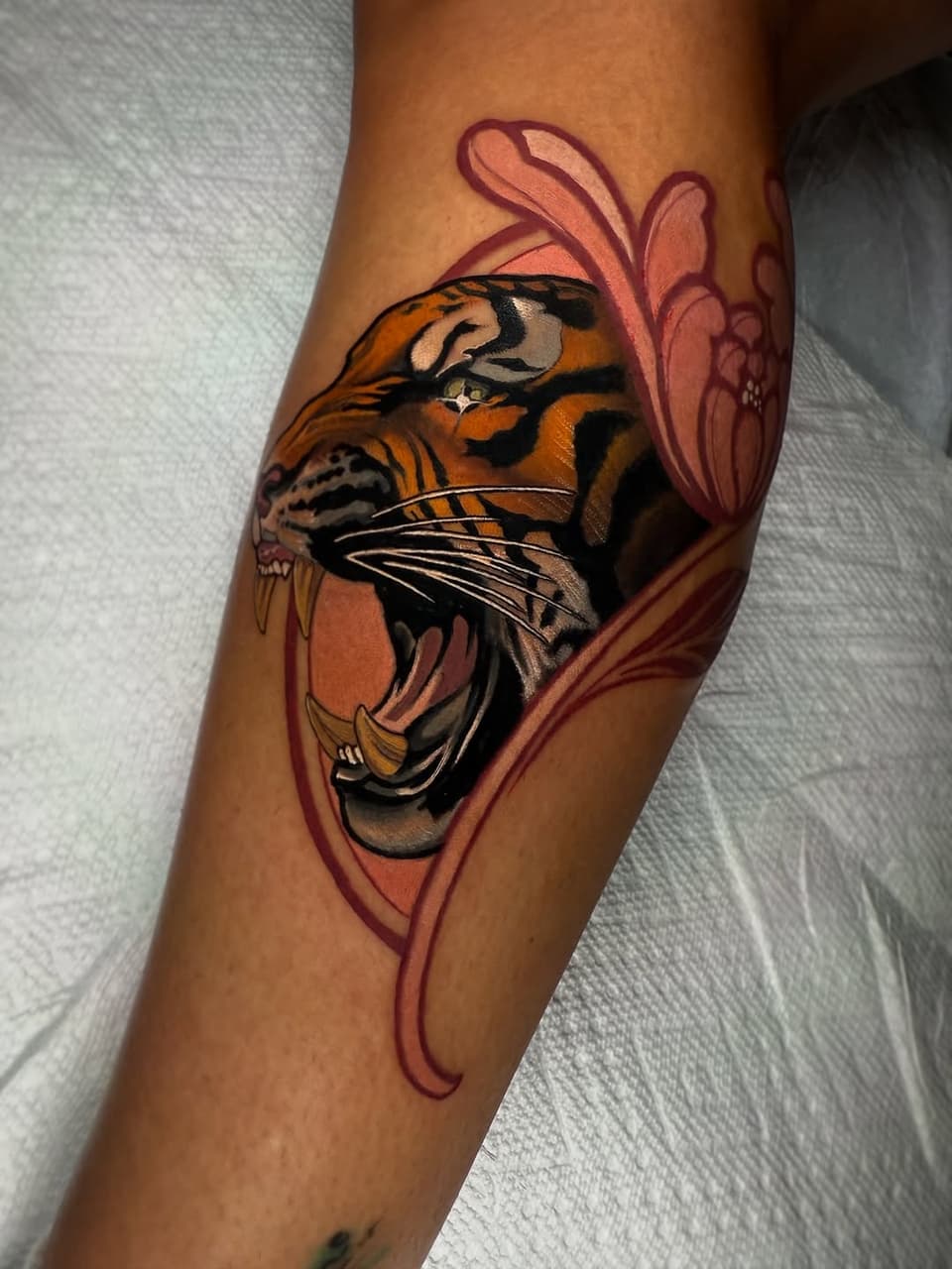 Tiger head with open mouth and pink floral design on upper arm, featuring orange, black, and white coloring with detailed facial features.