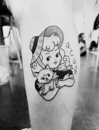 Vintage-inspired tattoo on thigh featuring a woman in a hat holding a smiling cat, with decorative lettering, rendered in black ink.