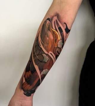 Colorful koi fish tattoo on a forearm featuring orange, yellow, black, and cream tones with detailed scales and fins.