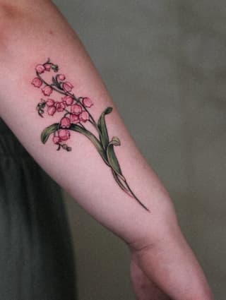 Delicate pink flower sprays with green stems and leaves tattooed on the upper arm, shown on light skin tone.