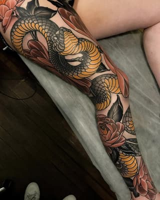 Full-leg tattoo sleeve featuring yellow and orange serpents with scaled details intertwined with red and pink flowers and black leaves on skin.
