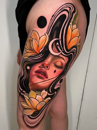 Woman's thigh tattoo featuring a female face with closed eyes, orange flowers, swirling black linework, and celestial elements in warm peachy and orange tones.