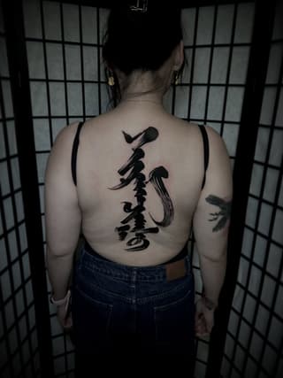 Back tattoo featuring a vertical black microphone with musical notes and abstract flowing lines down the spine.
