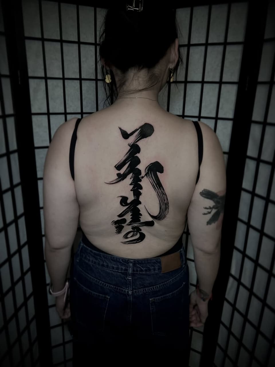 Back tattoo featuring a vertical black microphone with musical notes and abstract flowing lines down the spine.