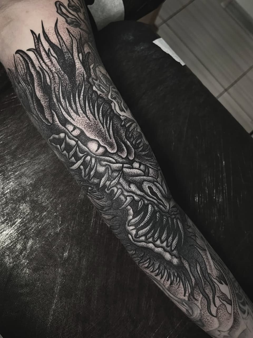 Detailed wing and feather tattoo covering the forearm with intricate linework and shading in black ink on pale skin.
