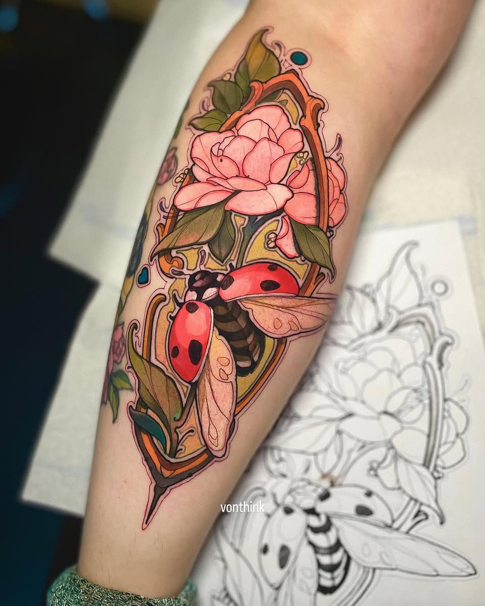 Colorful tattoo on a forearm featuring pink peonies, two red ladybugs with black spots, green leaves, ornamental scrollwork, and blue gemstones.