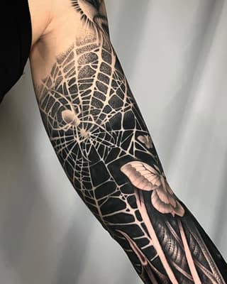 Intricate spider web and spiders tattoo on forearm with detailed shading, negative space details, and flesh-tone accents on black background.