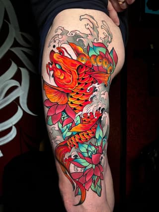 Colorful koi fish tattoo on thigh with red and orange scales, green leaves, white wave details, and decorative text elements.