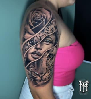 Shoulder tattoo featuring a woman's face with a rose and leopard head intertwined with ribbon wraps, rendered in grayscale on skin.