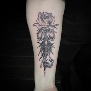 Vertical tattoo on pale forearm featuring a rose at top, bell-shaped flowers in middle, detailed insect with spotted center, and dripping element below in black ink.