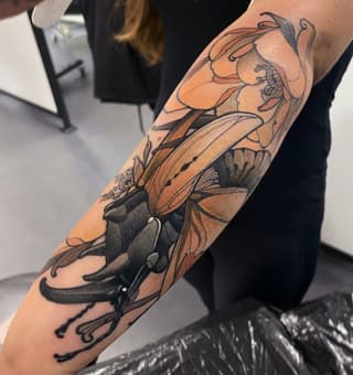 Detailed arm tattoo featuring layered insects including butterflies and beetles rendered in orange, tan, and black ink on the forearm.