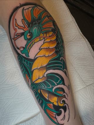 Colorful dragon tattoo on the calf featuring green and orange scales, decorative elements, and ornamental details with bold outlines.