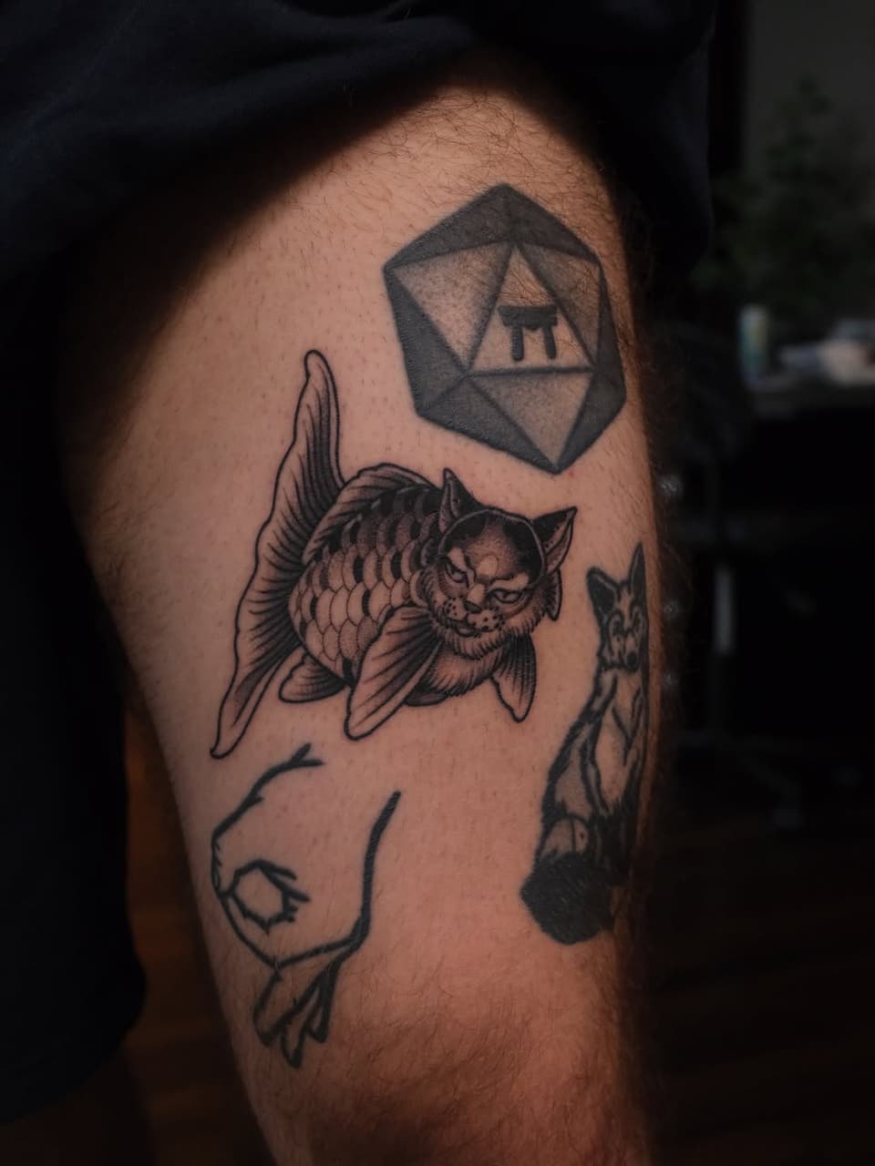 Tattoo on upper arm featuring a winged cat with detailed linework, a geometric polyhedron shape, and additional animal figures in black ink.